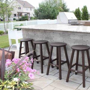 Outdoor kitchen bar with light granite countertops, stone block base, four bar stools, and a built-in grill, in a Wisconsin backyard