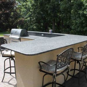 Outdoor bar with dark granite countertops, a light stucco base, built-in grill, and metal bar stools, on a paver patio