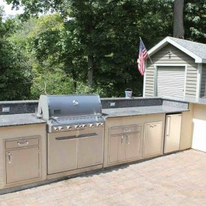 Outdoor kitchen with gray stone block base, dark granite countertops, built-in grill and refrigerator, on a paver patio